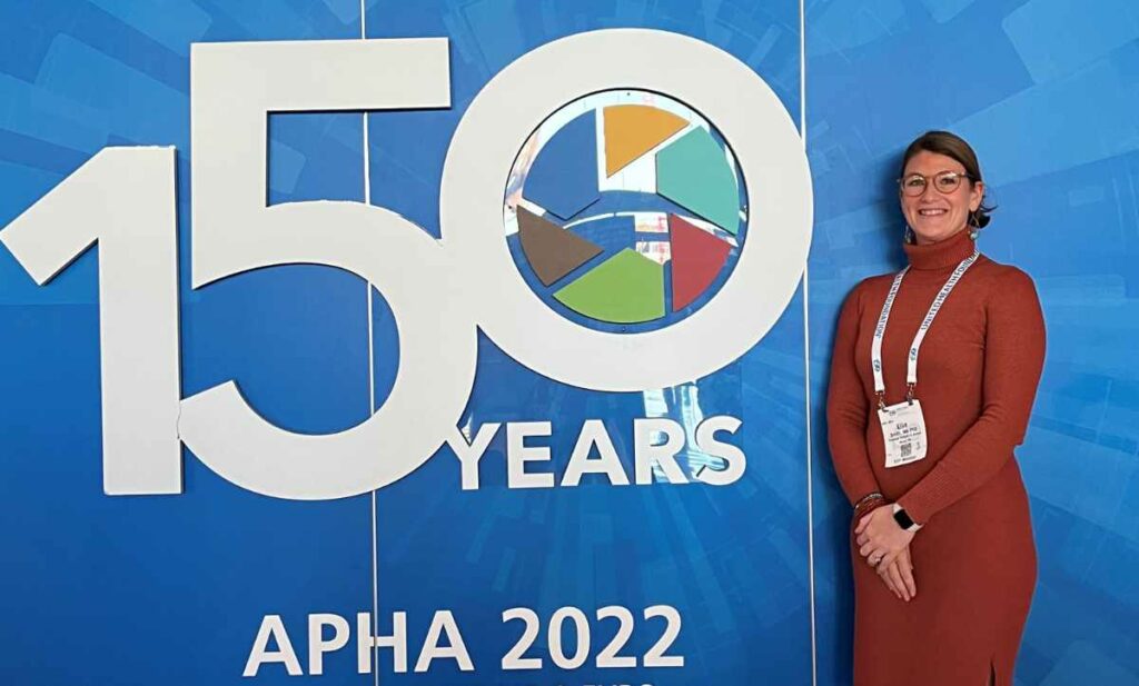 Ellie Smith standing in front of sign that says "150 Years: APHA 2022"